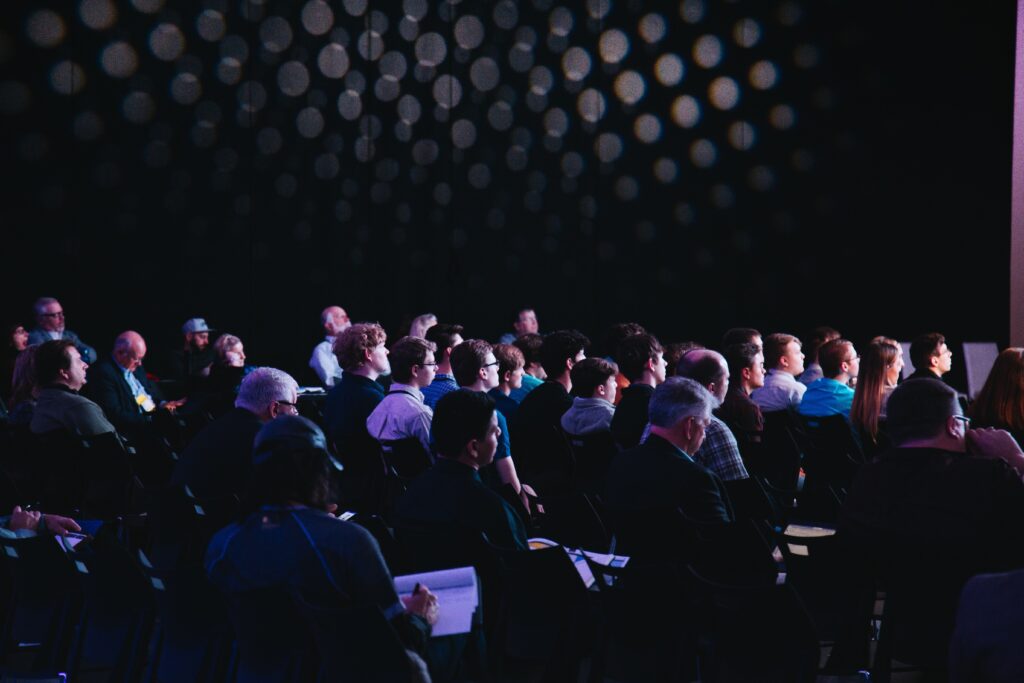 personas sentadas en una sala de eventos iluminadas por una pantalla